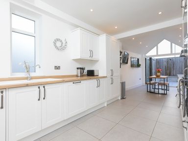 A kitchen with white cabinets wooden countertop and dining table with flowers at Captains Walk in Newquay