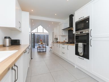A kitchen with white cabinets wood countertops a dining table and benches at Captains Walk in Newquay