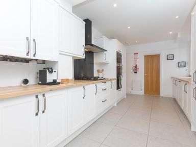 A kitchen with white cabinets wooden countertops and a wooden door at Captain's Walk in Newquay