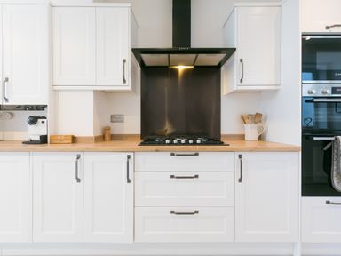 A kitchen with white cabinets a gas stove and black range hood at Captains Walk in Newquay