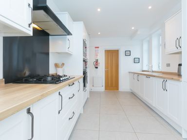 A kitchen with white cabinets wooden countertops a gas stove and a wooden door at Captains Walk in Newquay
