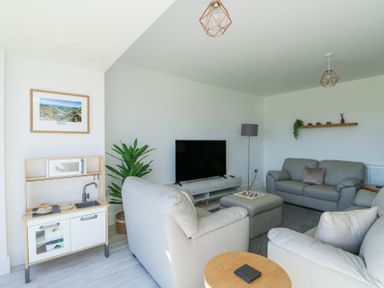 A living room with light colored sofas a television on a stand a small play kitchen and a plant at 6 Gwel Yr Wyddfa in Llanfaelog near Rhosneigr
