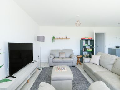 A living room with a television a gray rug a shelf with decor a floor lamp and beige sofas at 6 Gwel Yr Wyddfa in Llanfaelog near Rhosneigr