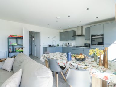 A kitchen and dining area with a table covered by a patterned tablecloth and a sofa nearby at 6 Gwel Yr Wyddfa in Llanfaelog near Rhosneigr