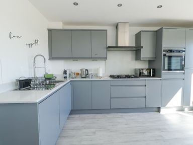 A modern kitchen with grey cabinets a built-in oven a gas stove a sink with a drying rack and a kettle on the counter at 6 Gwel Yr Wyddfa Llanfaelog near Rhosneigr