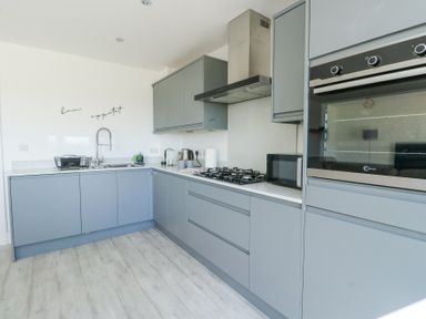A kitchen with gray cabinets a stainless steel oven a gas stove and a microwave at 6 Gwel Yr Wyddfa Llanfaelog near Rhosneigr