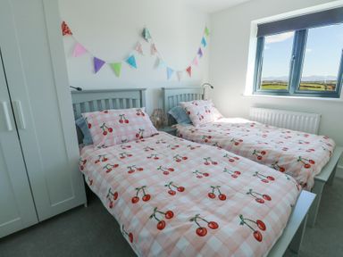 A bedroom with two single beds with cherry patterned bedding and a window showing a countryside view at 6 Gwel Yr Wyddfa Llanfaelog near Rhosneigr
