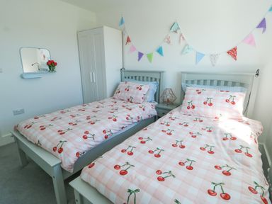 A bedroom with two single beds with cherry patterned bedding and a wardrobe and a mirror on the wall at 6 Gwel Yr Wyddfa Llanfaelog near Rhosneigr