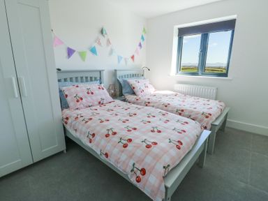A bedroom with two single beds featuring cherry patterned bedding and a window showing a countryside view at 6 Gwel Yr Wyddfa Llanfaelog near Rhosneigr
