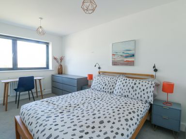 A bedroom with a double bed with polka dot bedding a bedside table with a lamp a dresser and a desk with a chair at 6 Gwel Yr Wyddfa Llanfaelog near Rhosneigr