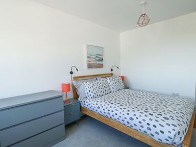 A bedroom with a bed with patterned bedding two bedside tables with lamps and a dresser at 6 Gwel Yr Wyddfa Llanfaelog near Rhosneigr