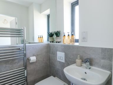 A bathroom with a sink toilet and window with soap dispensers and plants on the windowsill at 6 Gwel Yr Wyddfa in Llanfaelog near Rhosneigr
