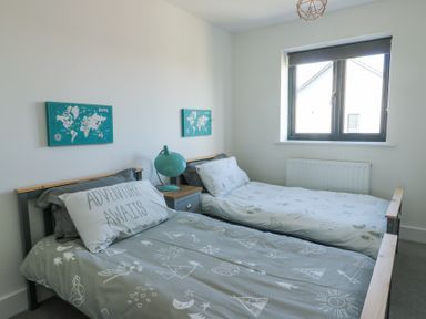 A bedroom with two single beds a bedside table and lamp and two world map pictures on the wall at 6 Gwel Yr Wyddfa Llanfaelog near Rhosneigr