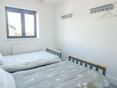 A bedroom with two single beds under a window and coat racks on the wall at 6 Gwel Yr Wyddfa in Llanfaelog near Rhosneigr