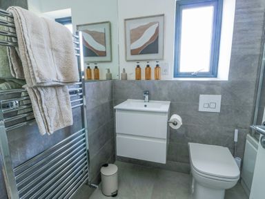 A bathroom with a wall-mounted sink and cabinet a toilet a heated towel rail with towels and a window at 6 Gwel Yr Wyddfa Llanfaelog near Rhosneigr