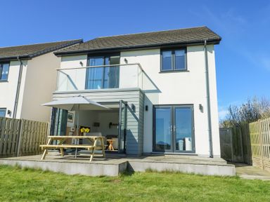 The back of a two story house with a patio door opening to a garden with a wooden picnic table and umbrella at 6 Gwel Yr Wyddfa Llanfaelog near Rhosneigr