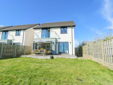 A backyard with a grass lawn fence and a two story house with a patio and outdoor table at 6 Gwel Yr Wyddfa in Llanfaelog near Rhosneigr