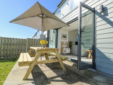 A patio area with a wooden picnic table and umbrella outside a house with glass doors at 6 Gwel Yr Wyddfa Llanfaelog near Rhosneigr