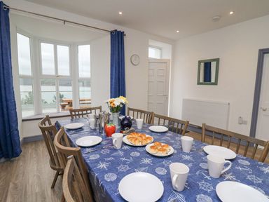 A dining room with a table set for breakfast and a bay window overlooking water at Fronwig in New Quay
