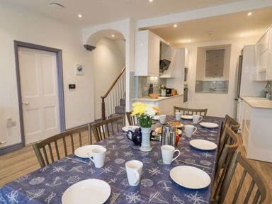 A dining table set with plates cups and a vase of flowers in a kitchen at Fronwig in New Quay