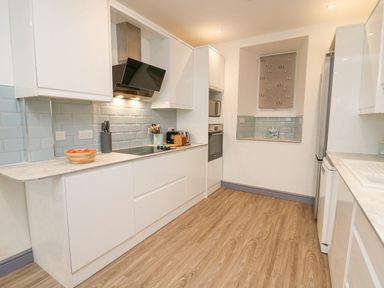 A kitchen with white cabinets a stove a bowl of tomatoes a toaster and a wooden floor at Fronwig in New Quay