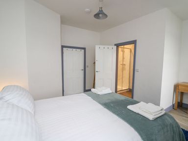 A bedroom with a bed and folded towels near two doors and a wooden table at Fronwig in New Quay
