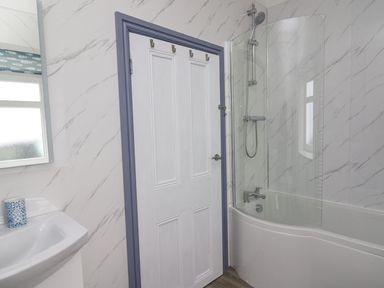 A bathroom with a white door next to a bathtub with a shower and a sink with a cup on it at Fronwig in New Quay