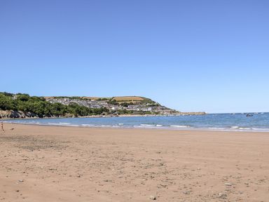 A sandy beach with scattered rocks and a town on a hill by the sea at Fronwig in New Quay