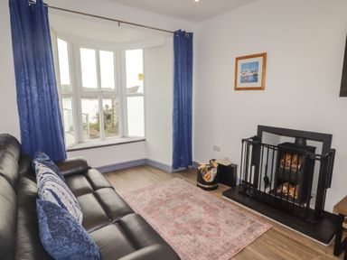 A living room with a black leather sofa blue curtains a bay window a fireplace with firewood and a rug on the floor at Fronwig New Quay