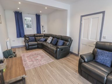 A living room with black leather sofas blue curtains and a pink rug at Fronwig in New Quay