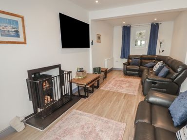 A living room with leather sofas a fireplace a wall mounted television and wooden floors at Fronwig in New Quay