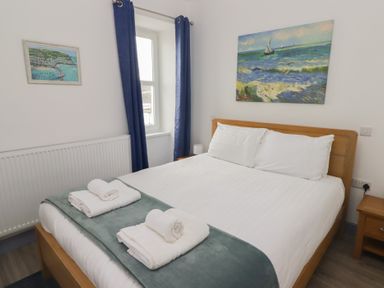 A bedroom with a double bed a wooden nightstand and paintings on the wall at Fronwig in New Quay