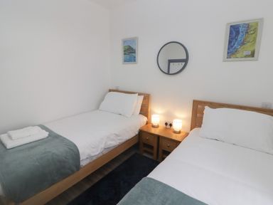 A bedroom with two single beds white bedding wooden furniture and a round mirror on the wall at Fronwig in New Quay