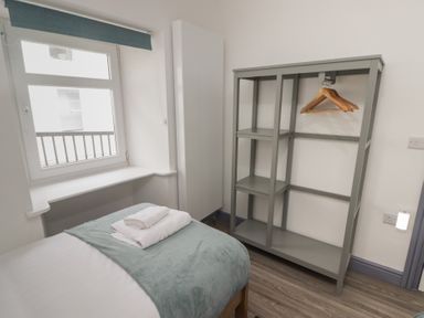A bedroom with a bed, folded towels on the bed, an open wardrobe with wooden hangers and a window at Fronwig in New Quay