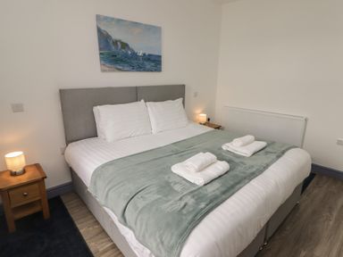 A bedroom with a double bed two bedside tables with lamps a painting on the wall and folded towels on the bed at Fronwig in New Quay