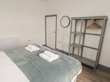 A bedroom with a bed with folded towels gray open wardrobe with hangers round wall mirror and closed door at Fronwig in New Quay