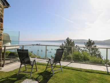 A balcony with two chairs overlooking a body of water with boats and hills in the distance at Fronwig in New Quay