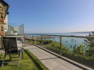 A balcony with two chairs overlooking a harbor with boats and a road below at Fronwig in New Quay