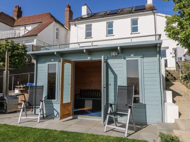 A small blue garden building with open double doors and two chairs outside at Fronwig in New Quay