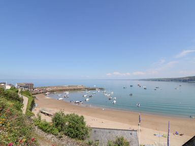 A sandy beach with people sunbathing a small harbor with boats and houses near the shore at Fronwig in New Quay