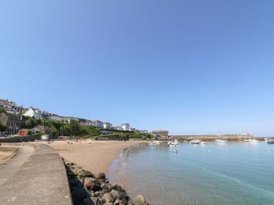 A beach with people on sand and boats on water near houses and a pier at Fronwig in New Quay