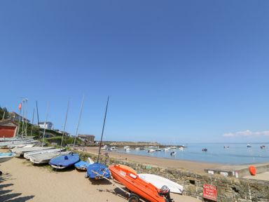 A sandy beach with small sailboats on the shore and boats in the water at Fronwig in New Quay