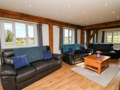 A living room with three black leather sofas with blue cushions and throws a wooden coffee table with a vase of flowers on a rug at Yr Adfa in Llangeitho near Tregaron