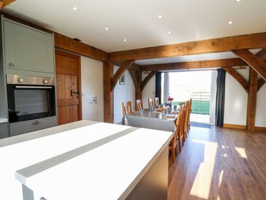 A dining area with a long table set with cups and plates wooden chairs exposed wooden beams and a kitchen oven at Yr Adfa in Llangeitho near Tregaron