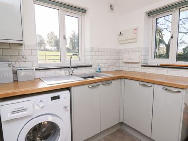 A kitchen corner with a washing machine under a wooden countertop and a double sink under two windows at Yr Adfa in Llangeitho near Tregaron