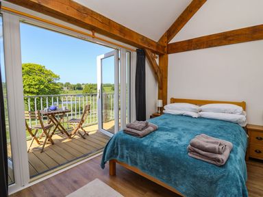 A bedroom with a double bed covered with a blue blanket and towels on top next to a balcony with wooden chairs and table at Yr Adfa in Llangeitho near Tregaron