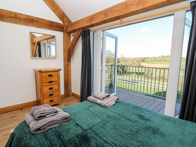 A bedroom with a wooden cabinet and a bed with towels on it and glass doors opening to a balcony with countryside view at Yr Adfa in Llangeitho near Tregaron