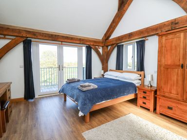 A bedroom with a wooden bed blue bedding wooden furniture and glass doors opening to a balcony at Yr Adfa in Llangeitho near Tregaron
