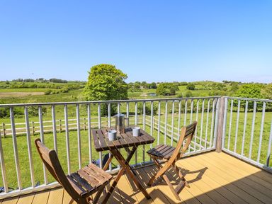 A balcony with two wooden chairs and a table with mugs and a thermos overlooking green fields and trees at Yr Adfa in Llangeitho near Tregaron