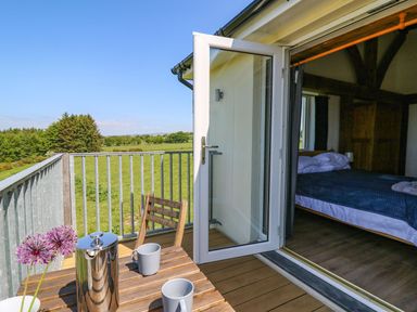 A balcony with a wooden table and chairs overlooking a green field and an open door leading to a bedroom at Yr Adfa in Llangeitho near Tregaron